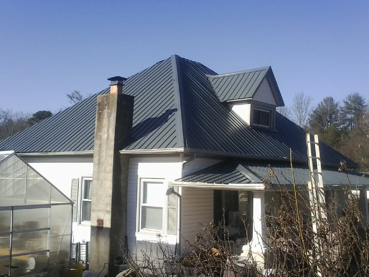 Dark blue standing seam metal roof on a white farmhouse with dormer — Slate & Tile Roof Repair by Roofing Brothers in Bridger