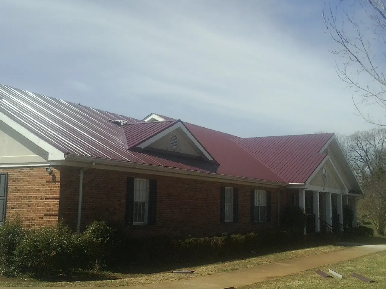Red metal roof with gabled entries on a long brick building, from a Hail Damage Roof Repair job in Bridger