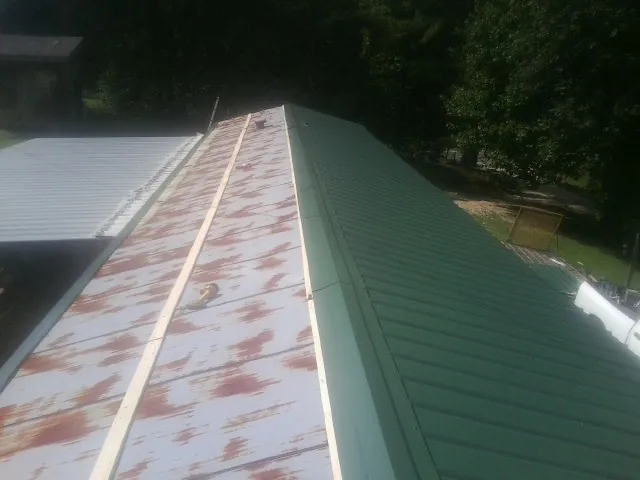 Old rusted panels beside newly installed green metal roofing — Wind Damage Roof Repair by Roofing Brothers in Bridger