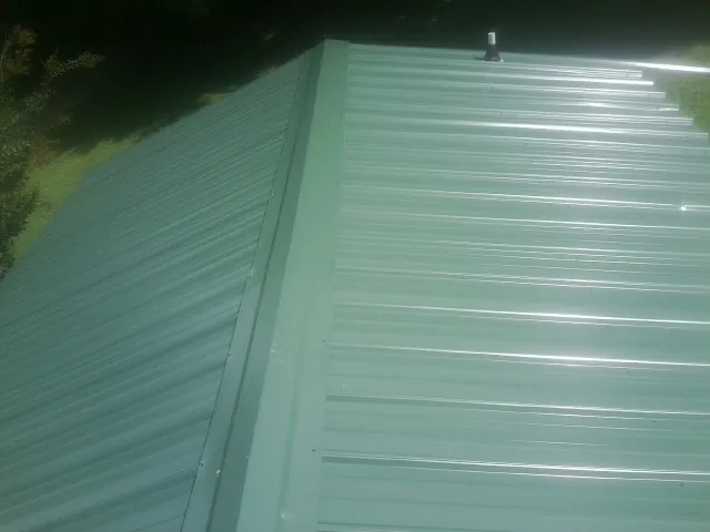 New green metal panels meeting at the ridge of a roof — Flat Roof Repair work by our crew in Bridger