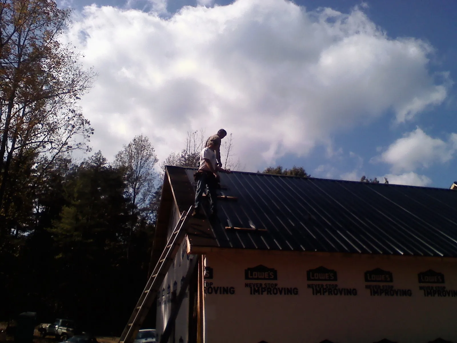 Roofer fastening dark metal panels high against a cloudy sky, from a Roof Inspection job in Bridger