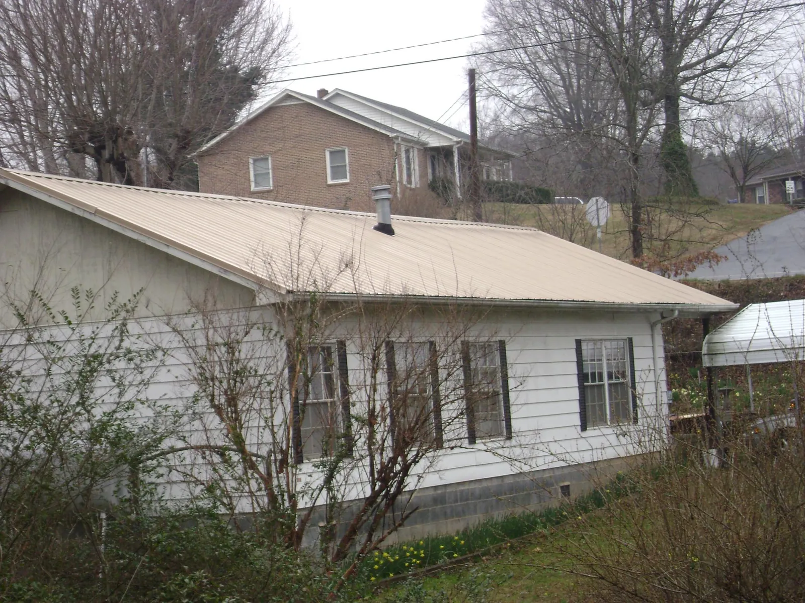 Tan metal roof on a white sided house set into a hillside — Commercial Roofing by Roofing Brothers in Bridger